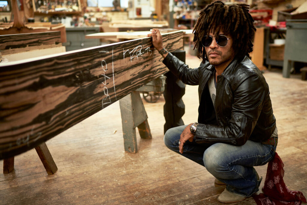 Lenny Kravitz crouching next to the Kravitz Grand Piano