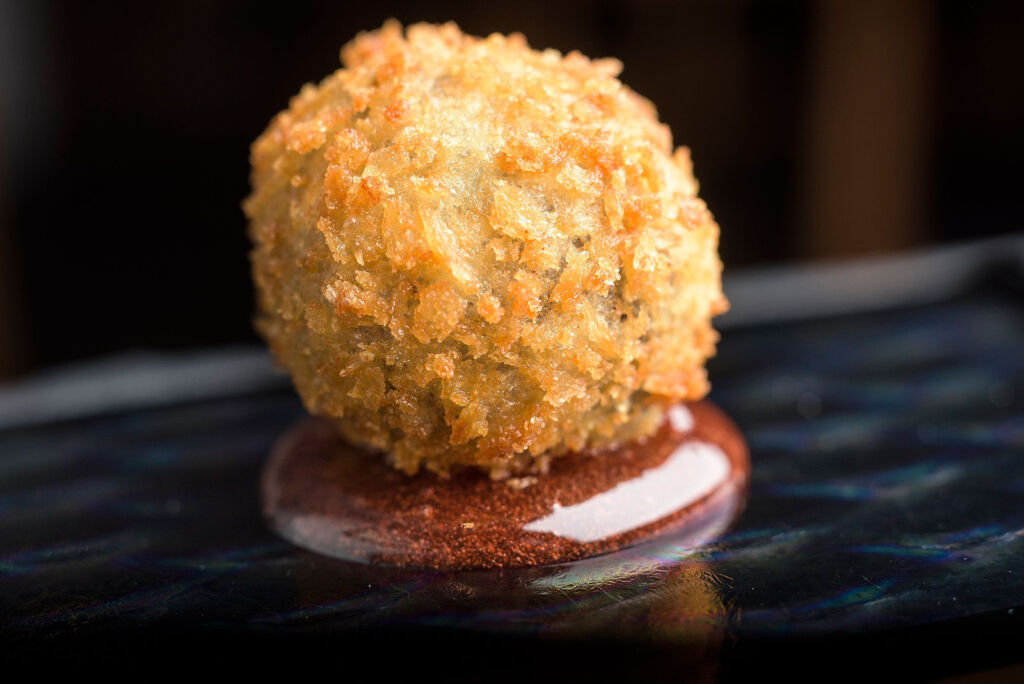 A unique circular shaped take on black pudding, coated i breadcrumbs and one a circle of sauce