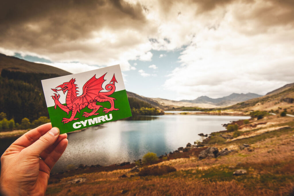 Holding up a card with CYMRU on it with the Welsh Dragon with stunning Welsh scenery behind it.