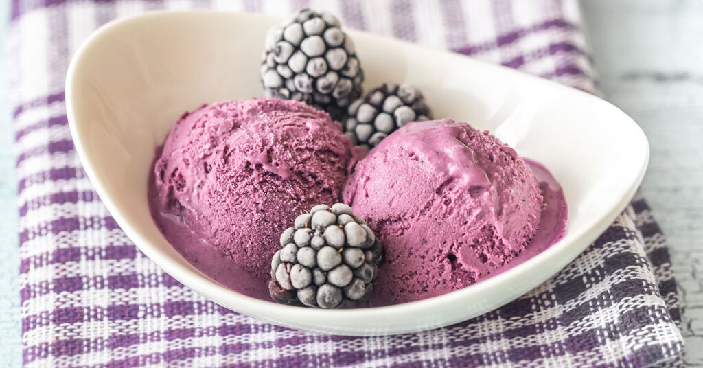 A bowl of blackberry ice cream with some frozen blackberries