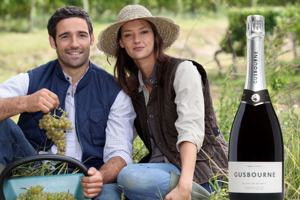 A couple holding a bunch of grapes next to a bottle of the vineyards Blanc de Blancs