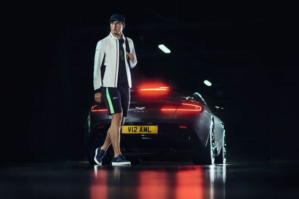 A male model wearing some of the new collection in front of an Aston Martin car