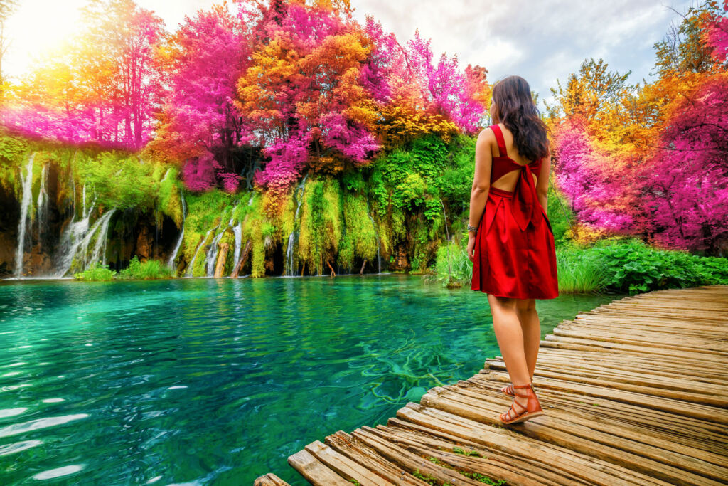 A woman standing on a jetty surrounded by the incredible natural colour of the foliage