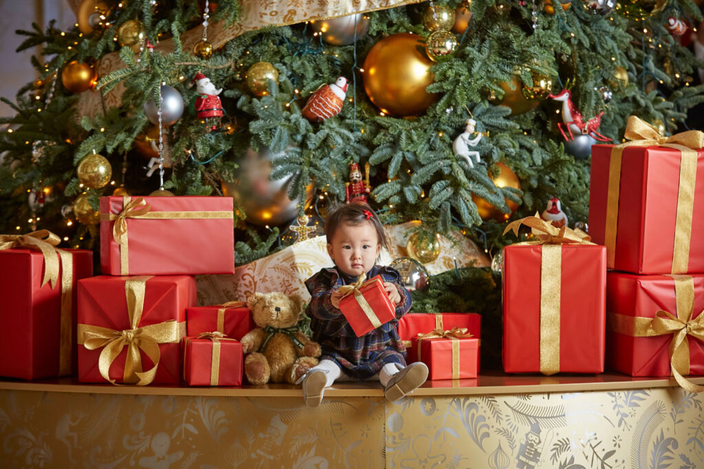 A young child among Christmas presents next to a tree