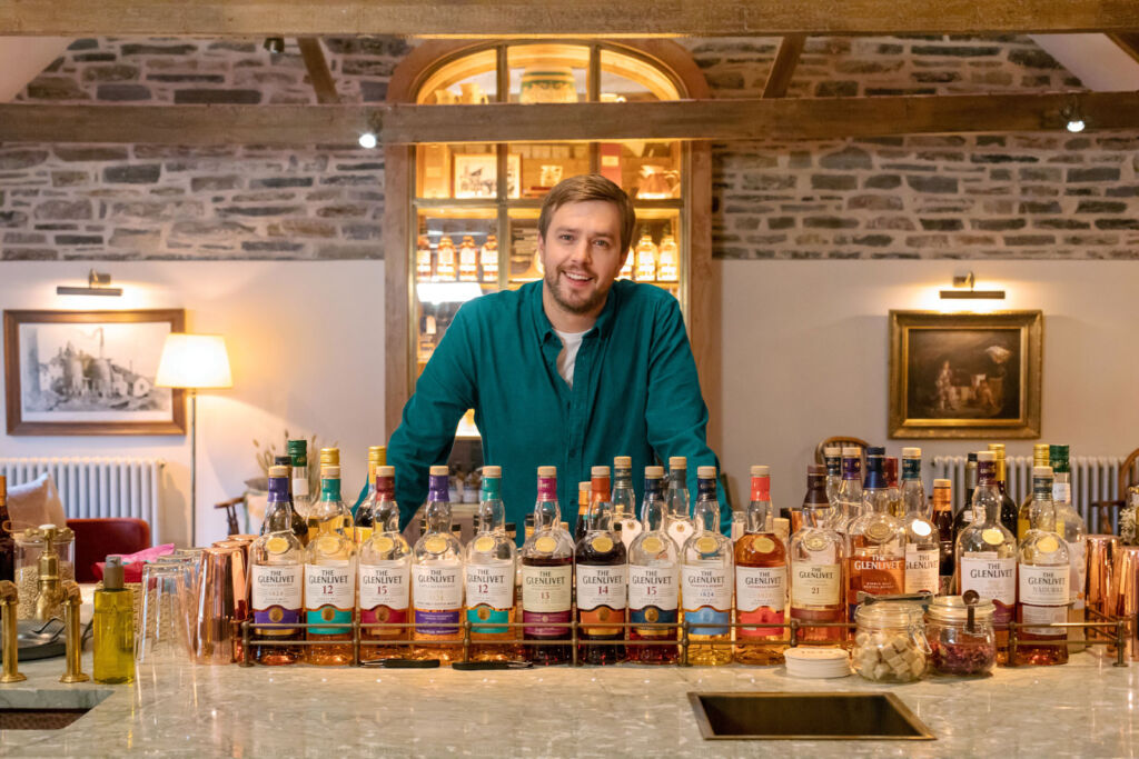 Iain Stirling standing in front of a vast array of bottles in the drawing room