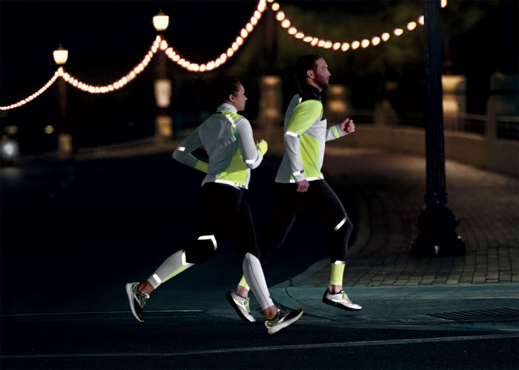A man and a woman running at night wearing the Brooks Run Visible Collection