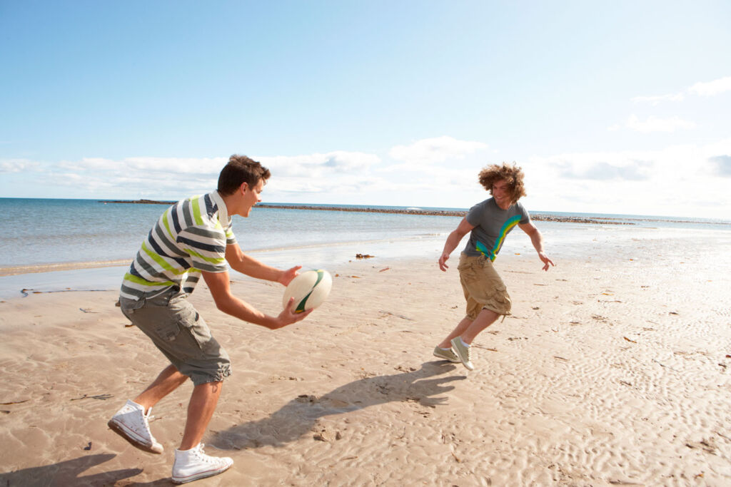Young men playing rugby on a beach