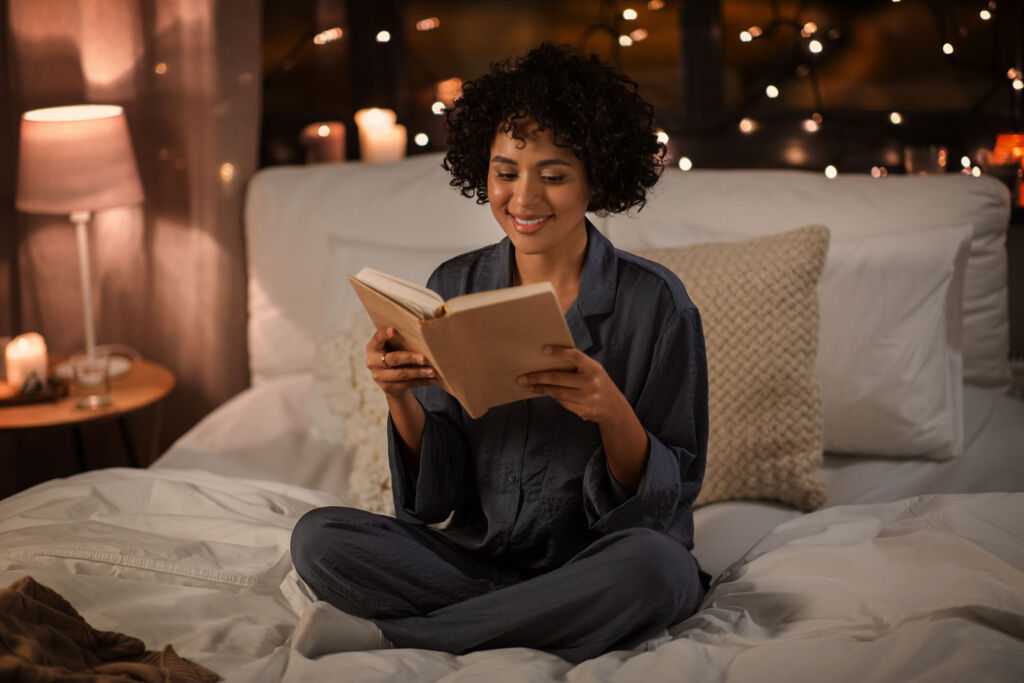 A woman reading a book on her bed at night time before going to sleep