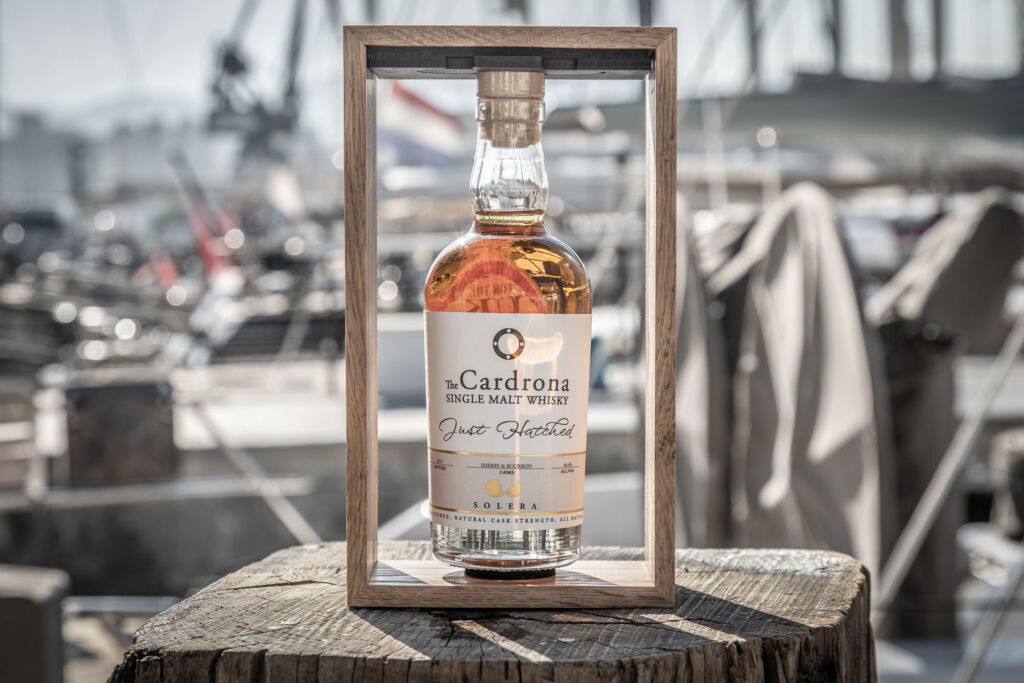 A bottle of the Just Hatched Solera Single Malt in a boat marina
