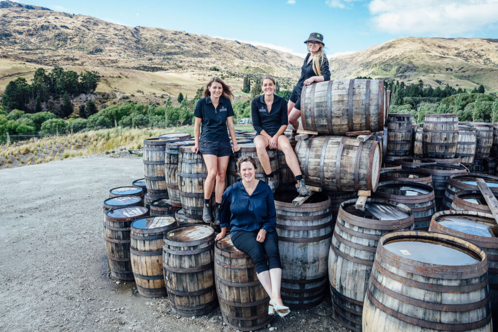 The female members of the team sat on some barrels outdoors