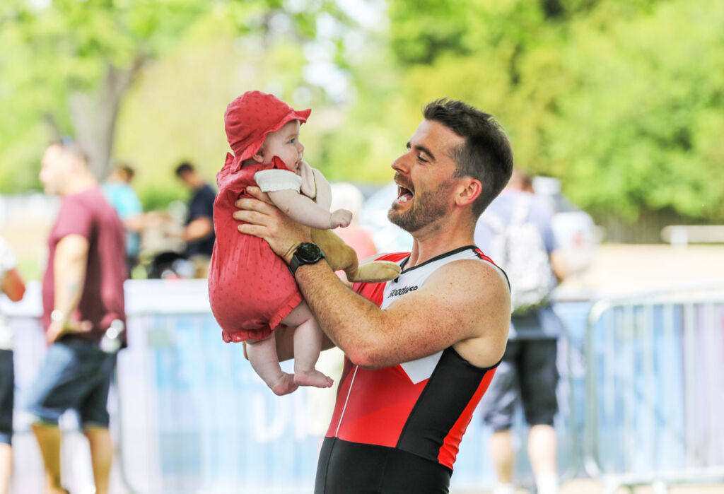 A man celebrating with his baby at the Blenheim Palace Triathlon