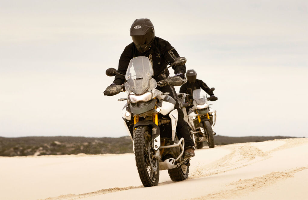 Two of the motorcycles being ridden on soft sand