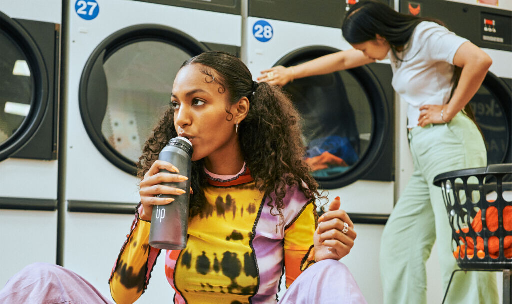 A woman sat down in a launderette drinking from the bottle