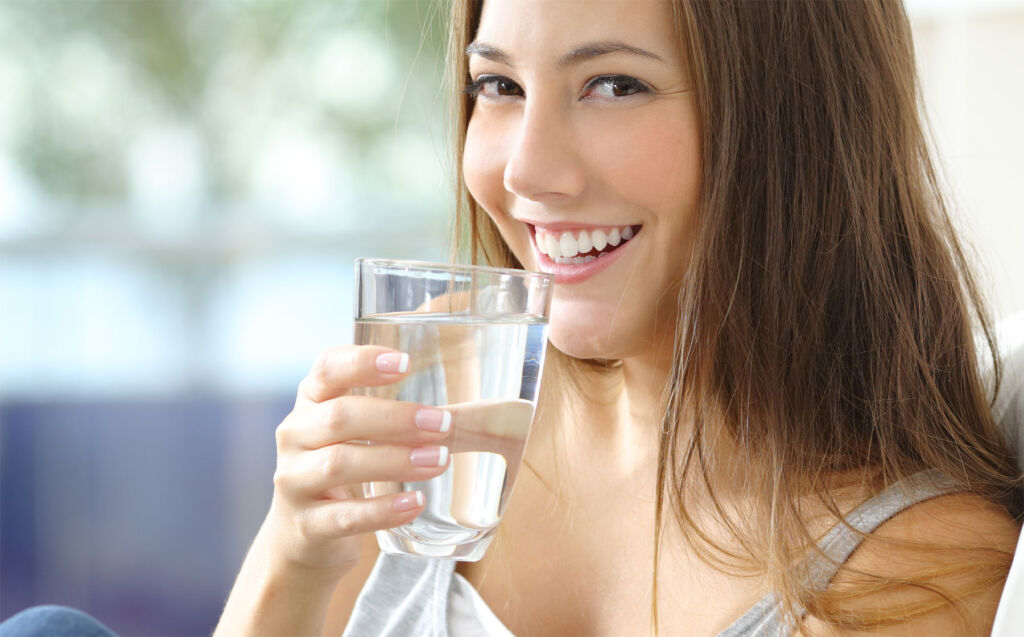 A young woman drinking water to hydrate her skin