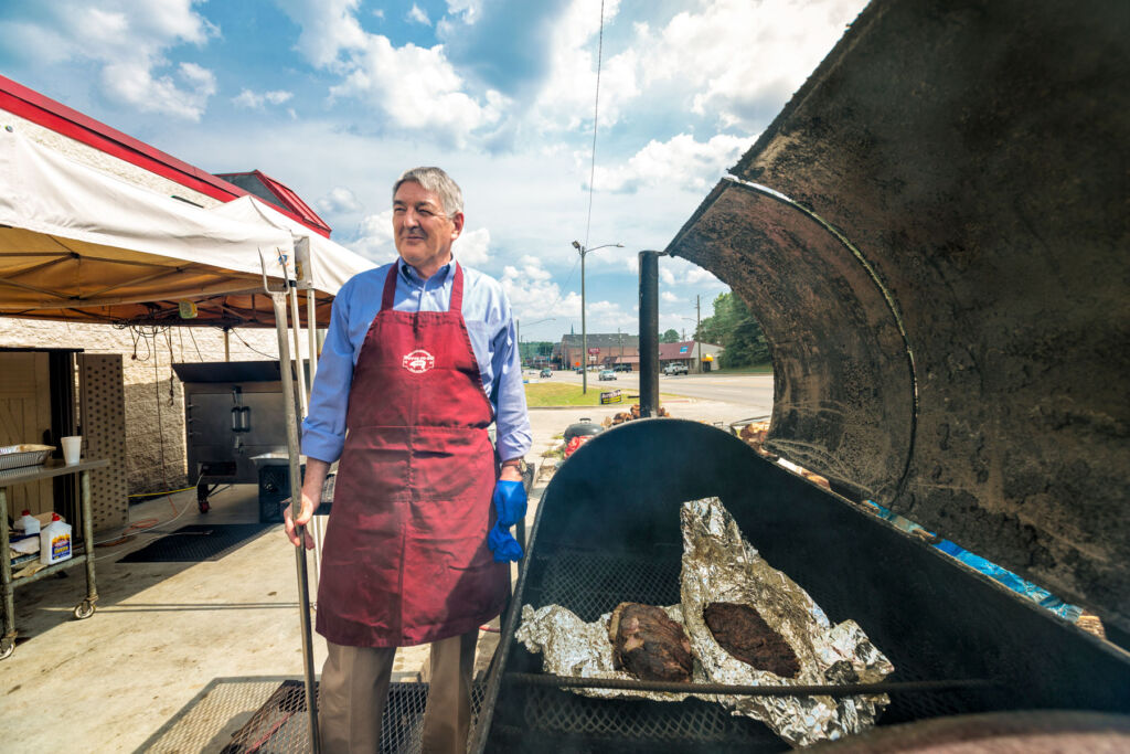 An older man cooking meat in a barbecue at Butts to Go
