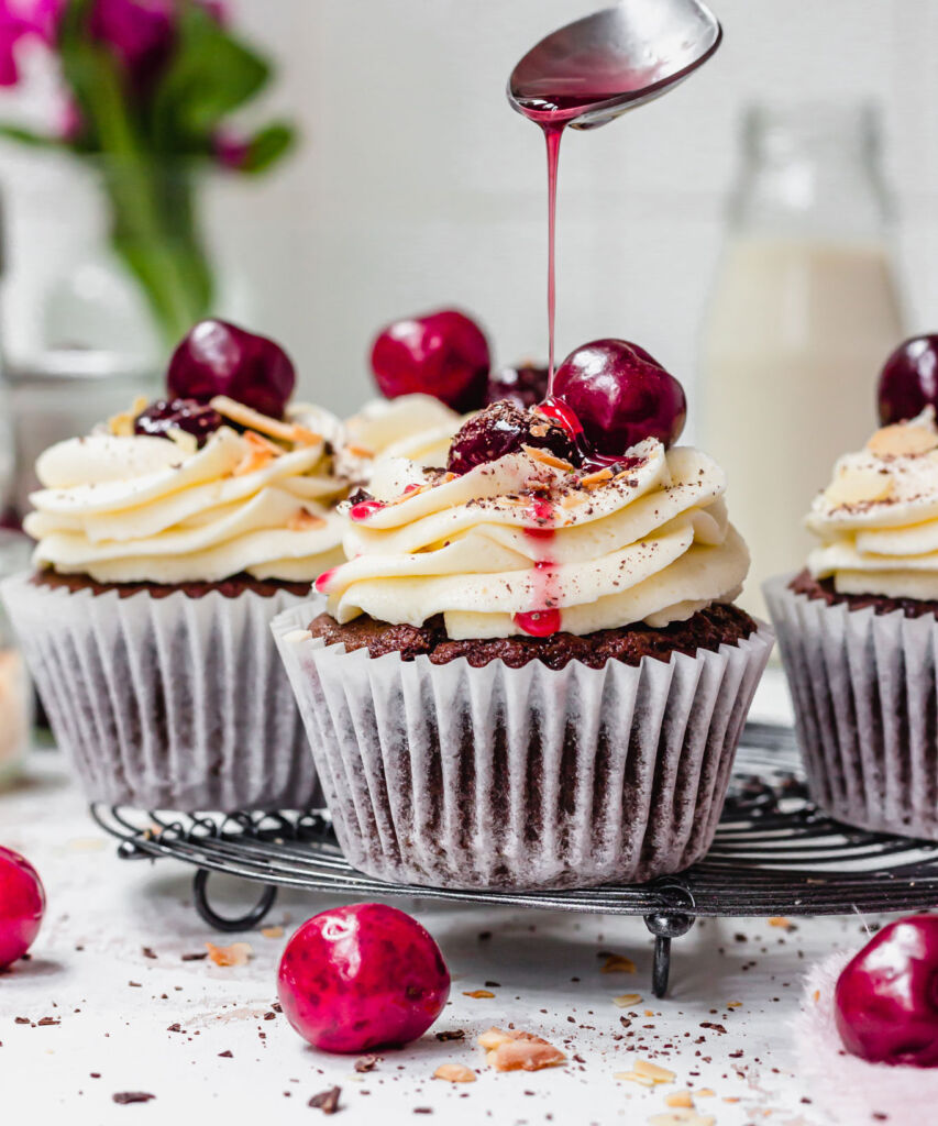 Chocolate Cherry Amaretto Cupcakes being drizzled with a topping from a spoon