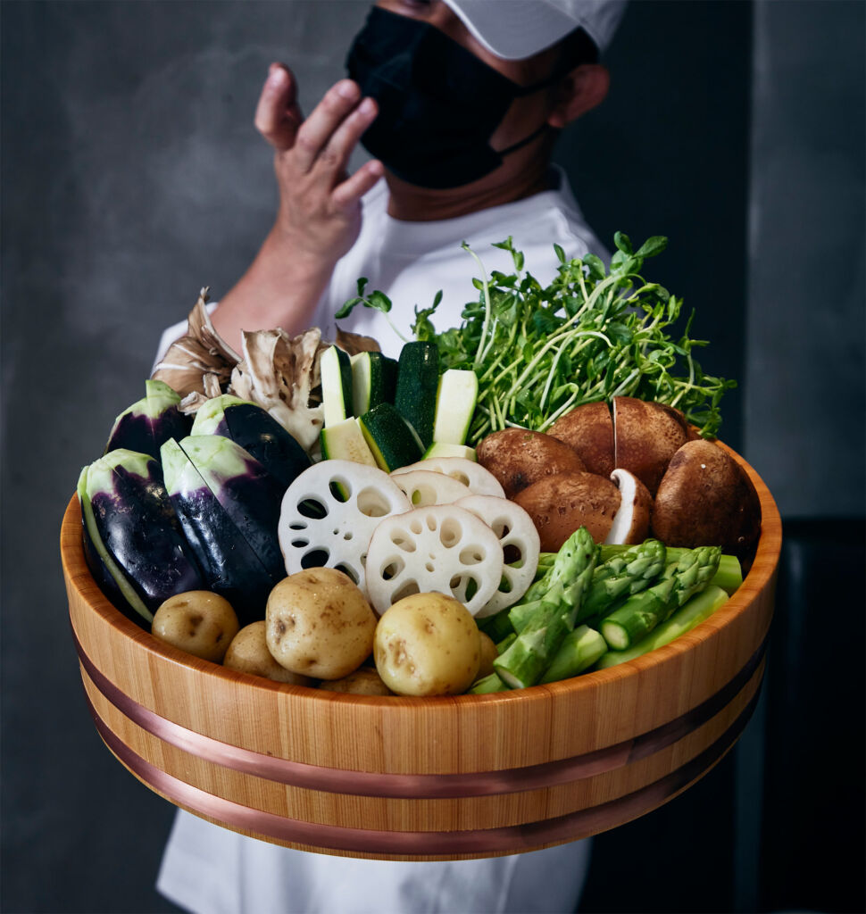 A member of the team holding a wooden tray stacked with fresh vegetables