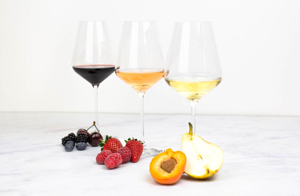 Three varieties of wine with fruits next to them to denote their flavours
