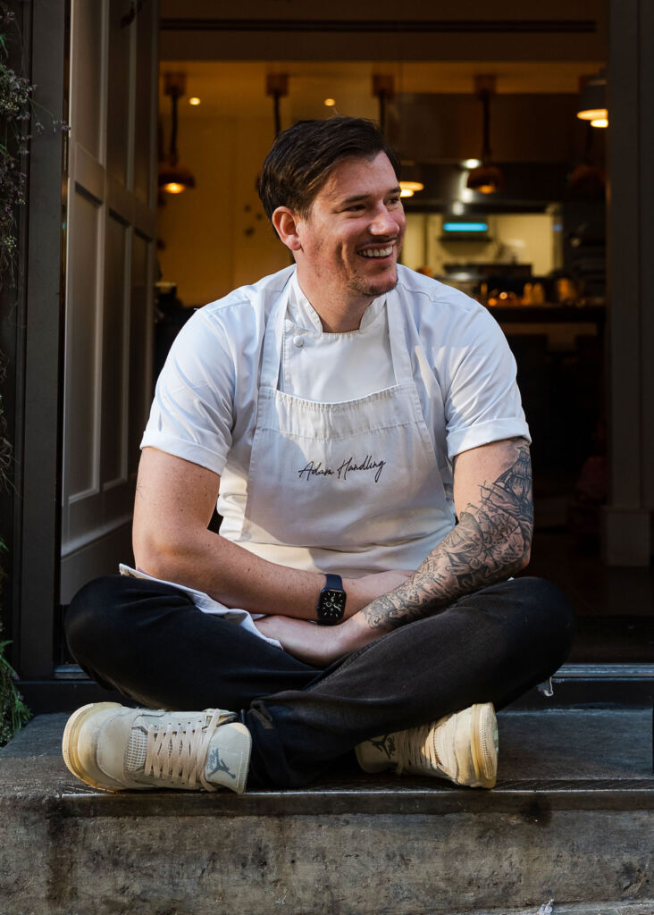 Chef Adam, sat cross-legged outside one of his restaurants