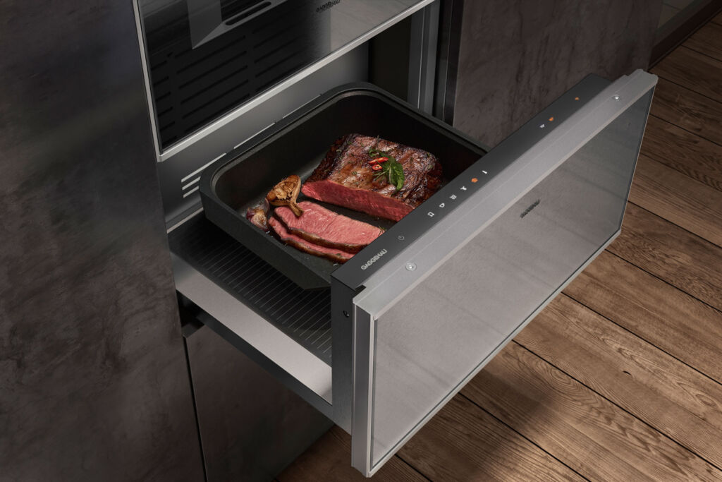A bare metal coloured drawer, open with food inside being warmed