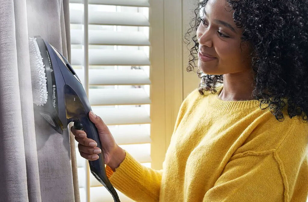 A woman cleaning her curtains with the Russell Hobbs Steam Genie 2-in-1 Handheld Steamer
