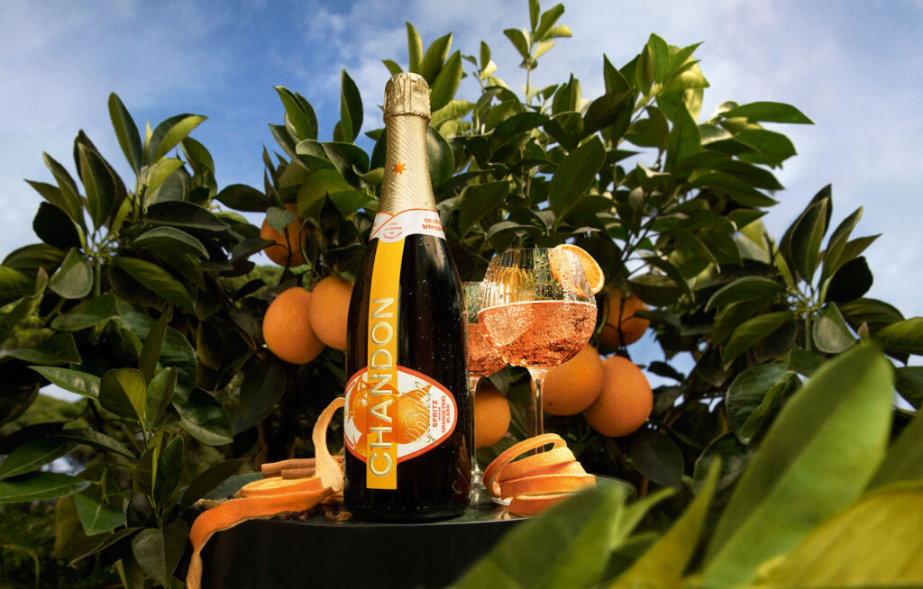 A bottle of Chandon Garden Spritz next to an orange fruit tree