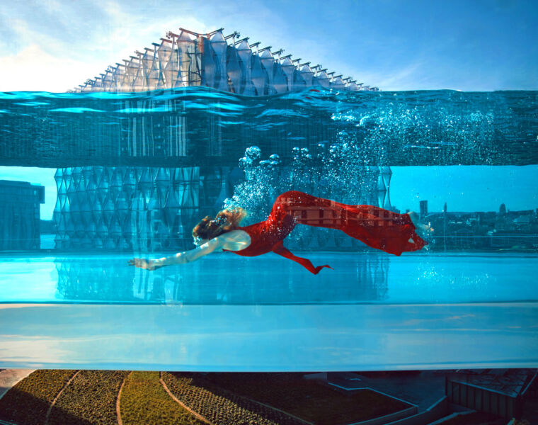 A woman swimming in the Embassy Gardens Sky Pool in a red dress