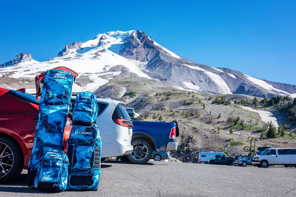 The ski and snowboard bags in a car park next to a snow capped mountain