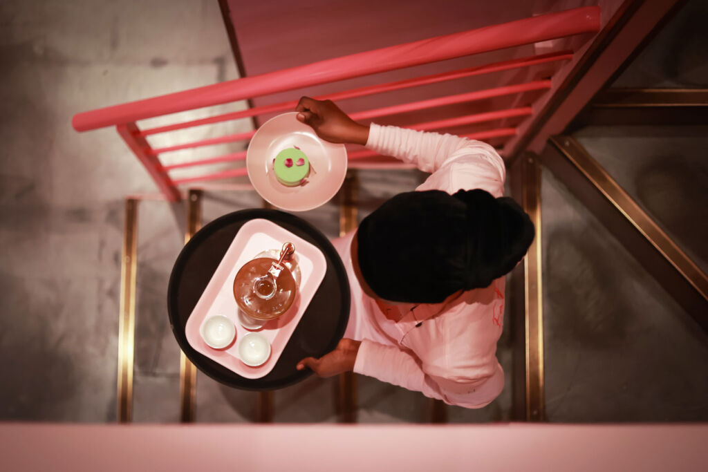 A member of staff carrying a tray of food down the bright pink staircase