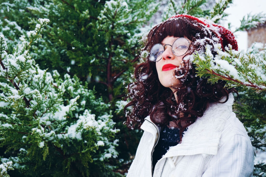 A woman wearing glasses by some snow covered trees