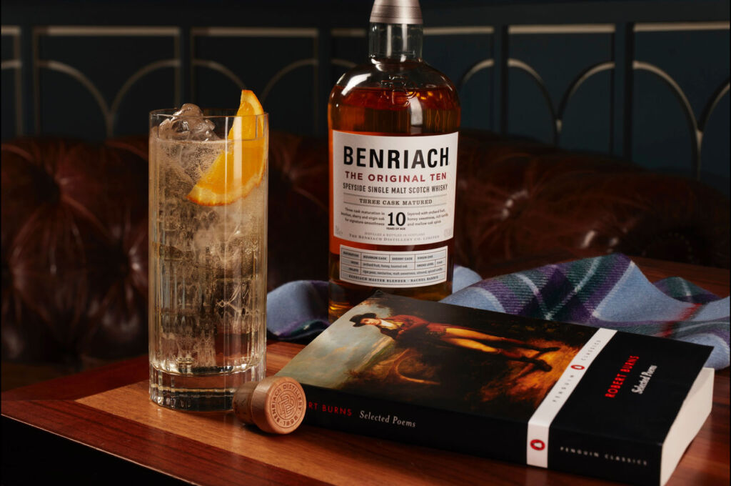A bottle of the whisky on a table with a full glass and a book