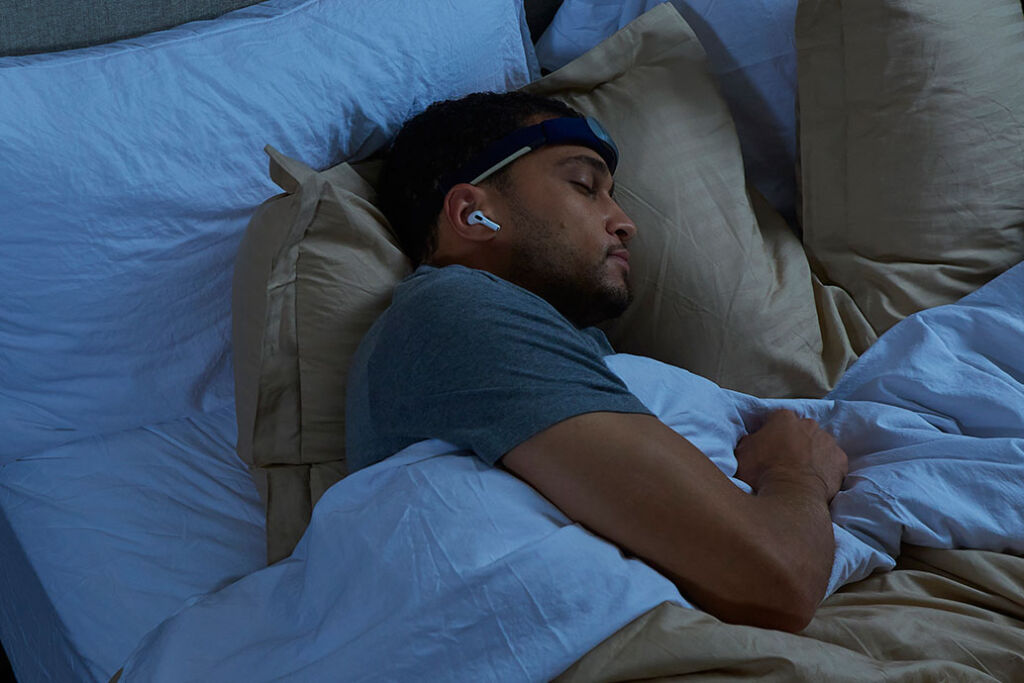 A man sleeping in his bed wearing a headband to monitor the quality of his sleep