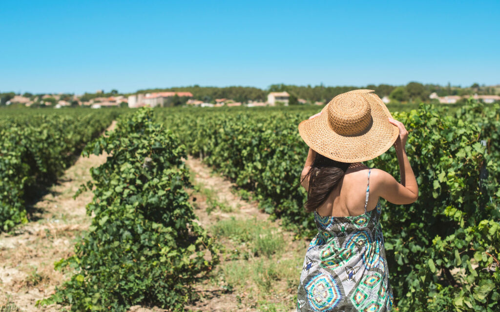 A woman wearing a hat walking through a vineyard in Tuscany