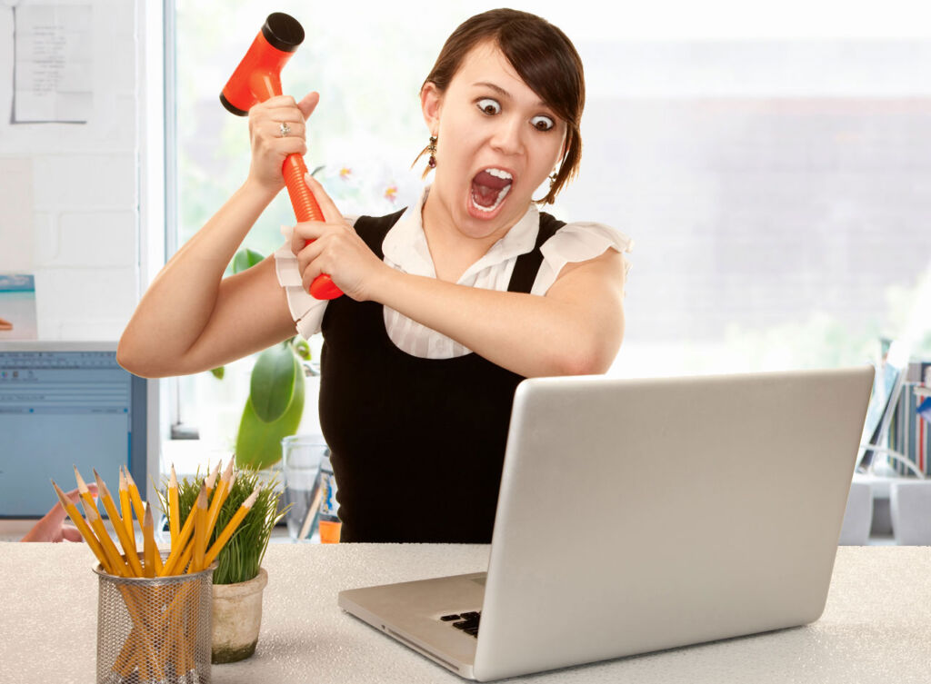 A young woman hitting her computer with a hammer