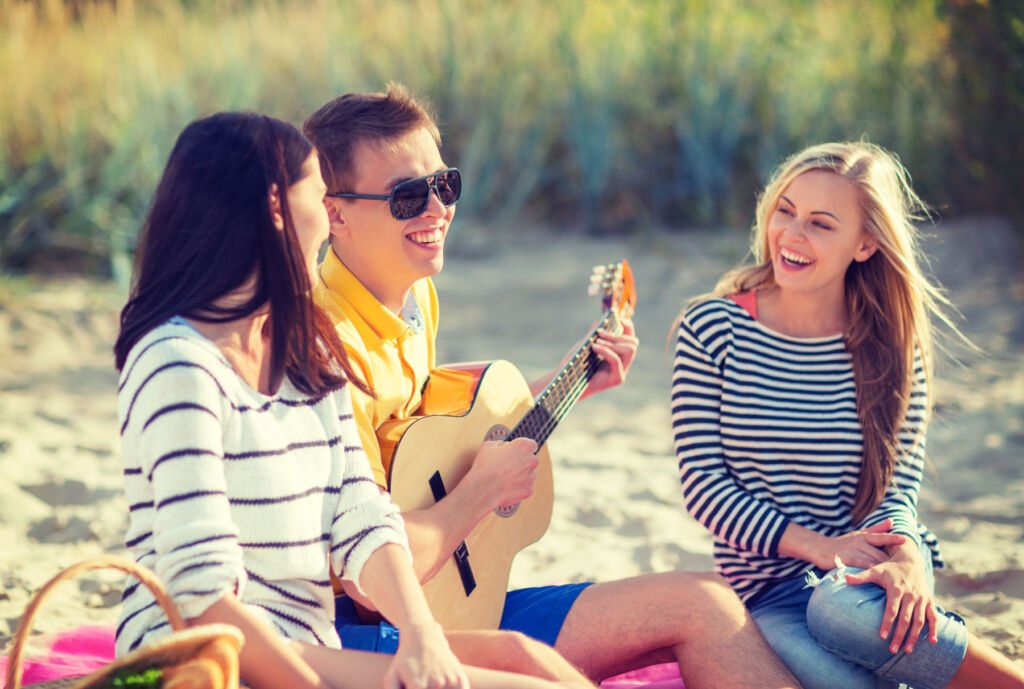 A young man serenading ladies on the beach with his guitar