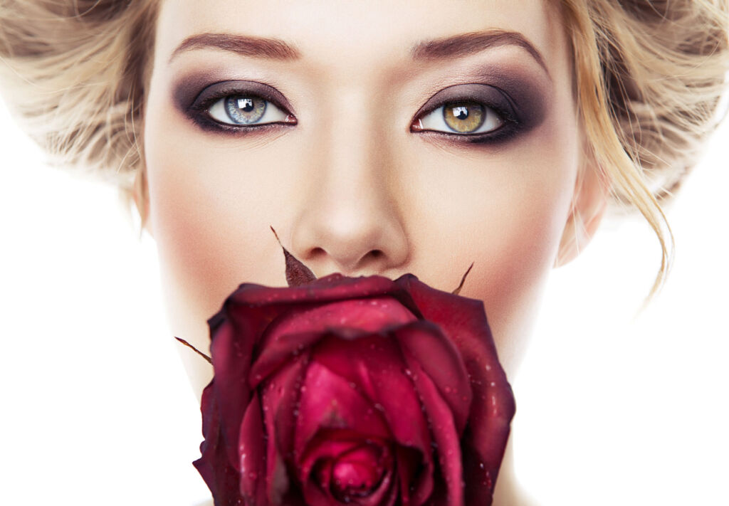 A blonde haired woman smelling a red rose