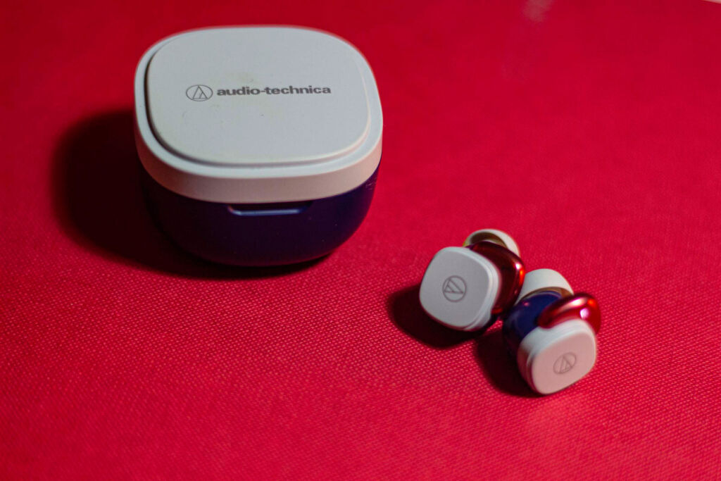 A set of grey coloured earphones next to its box on a red table
