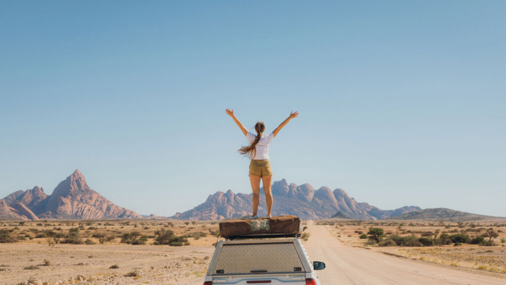 A woman standing on top of her car roof holding her arms out in celebration