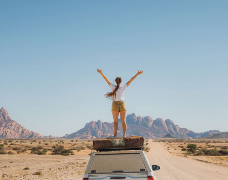 A woman standing on top of her car roof holding her arms out in celebration
