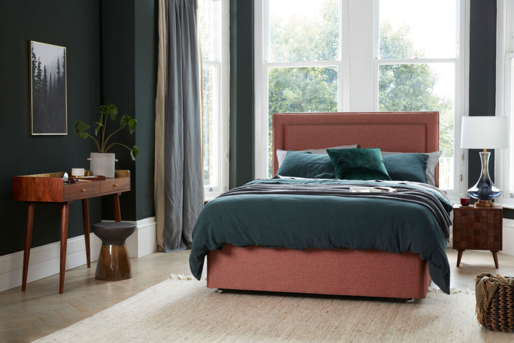 A dark pink coloured bed with green bedding