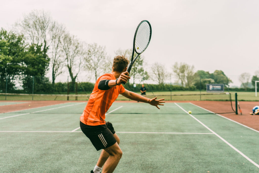 A young man dressed in orange playing with a modern racquet