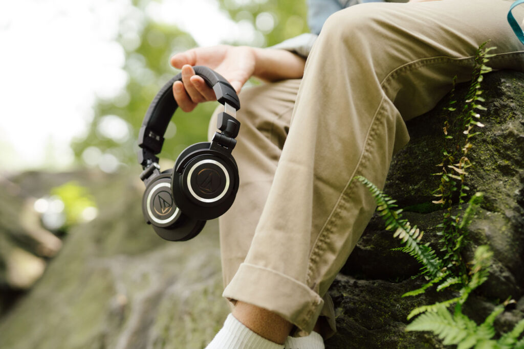 A person outdoors sat on a rock with the headphones in their hand