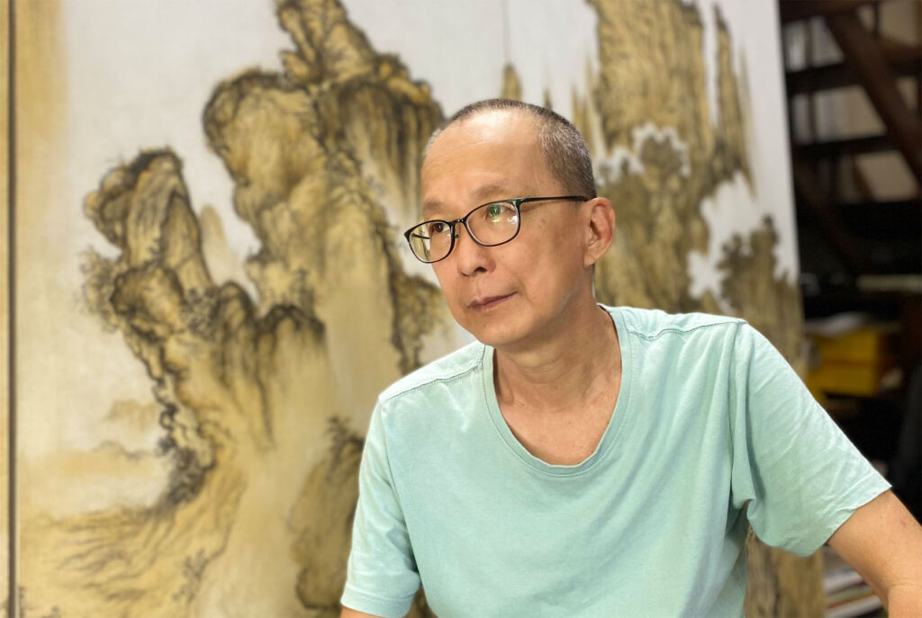 Chen Wei Meng sitting in front of one of his landscape paintings
