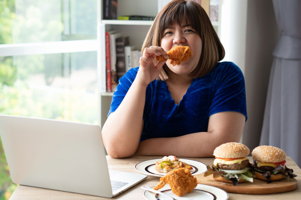 An overweight woman eating fried chicken and burgers