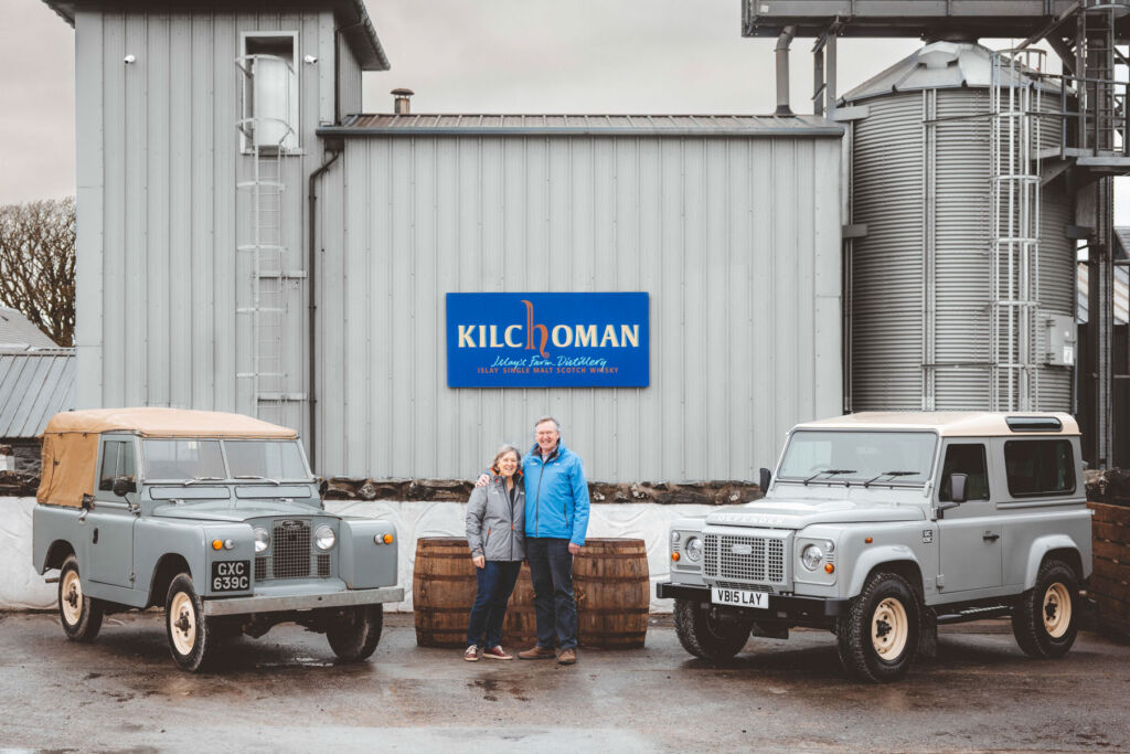 Kathy and her husband outside the distillery next to the original estate Land Rover and the special edition new version