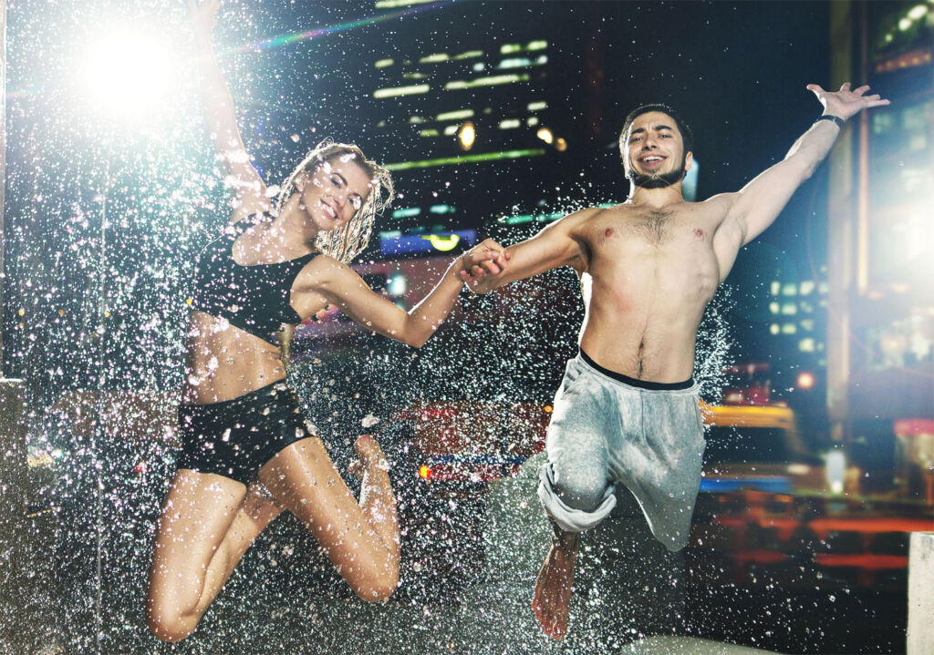A couple jumping with joy in the rain on a rooftop