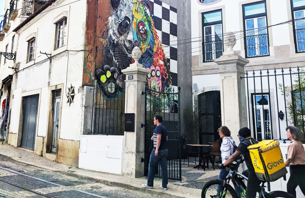 People walking by some street art whcih depicts a panda with one half of its face painted black and white and the other multi-coloured