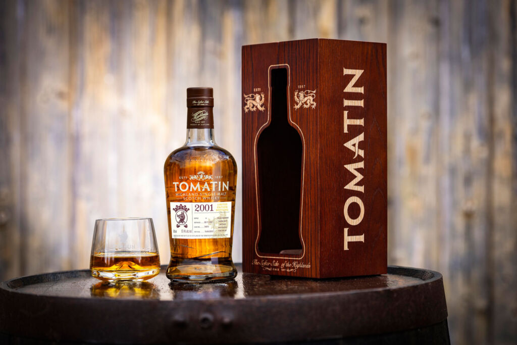 A bottle of the Tomatin whisky on a wooden barrel, next to its box and a part-filled glass