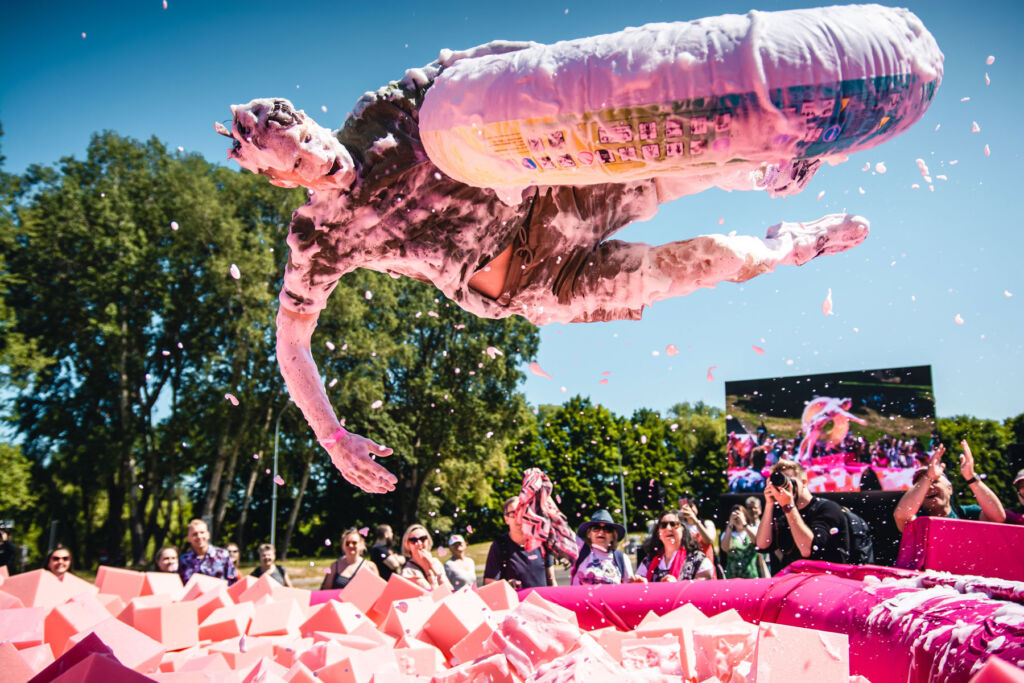 A young man covered in pink foam flying into the giant bowl of pink soup