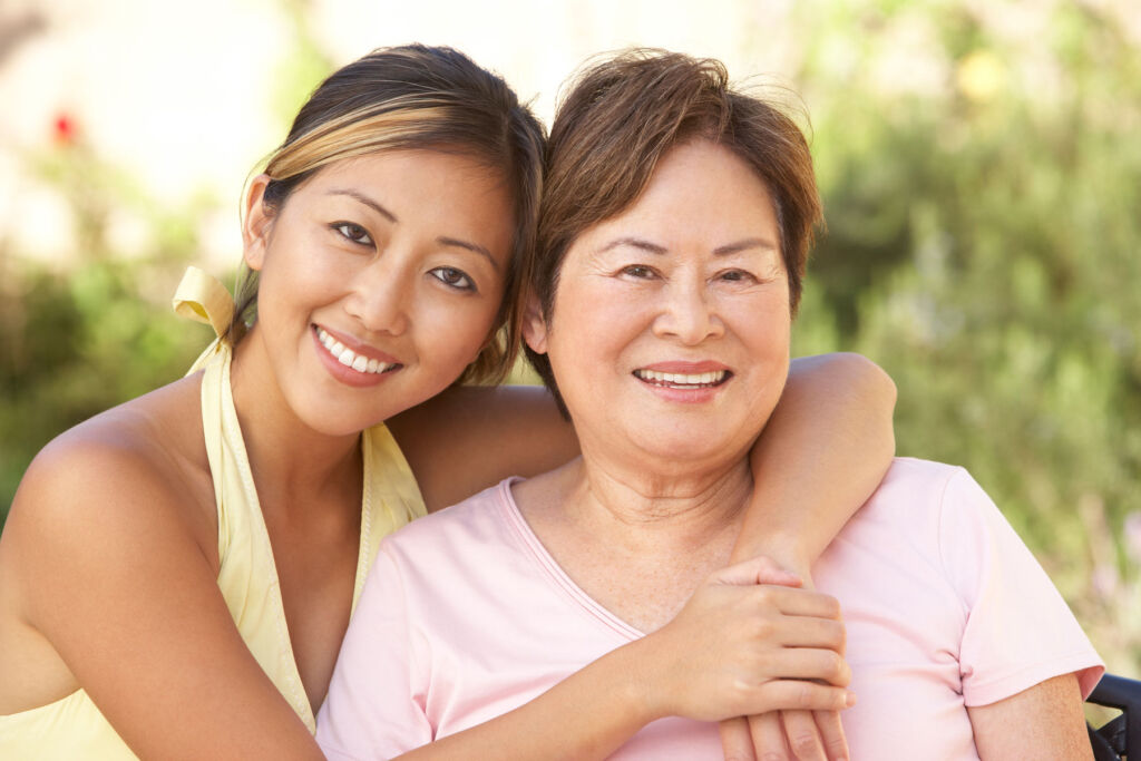 An attractive young woman with her arms draped over an older woman who is ageing gracefully
